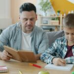 Vater und Sohn lernen zusammen. Der Vater zeigt das Lehrbuch, der Sohn schreibt. vitaly-gariev-Fmgn4q1aqsc-unsplash