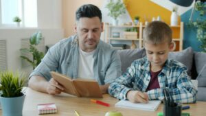 Vater und Sohn lernen zusammen. Der Vater zeigt das Lehrbuch, der Sohn schreibt. vitaly-gariev-Fmgn4q1aqsc-unsplash